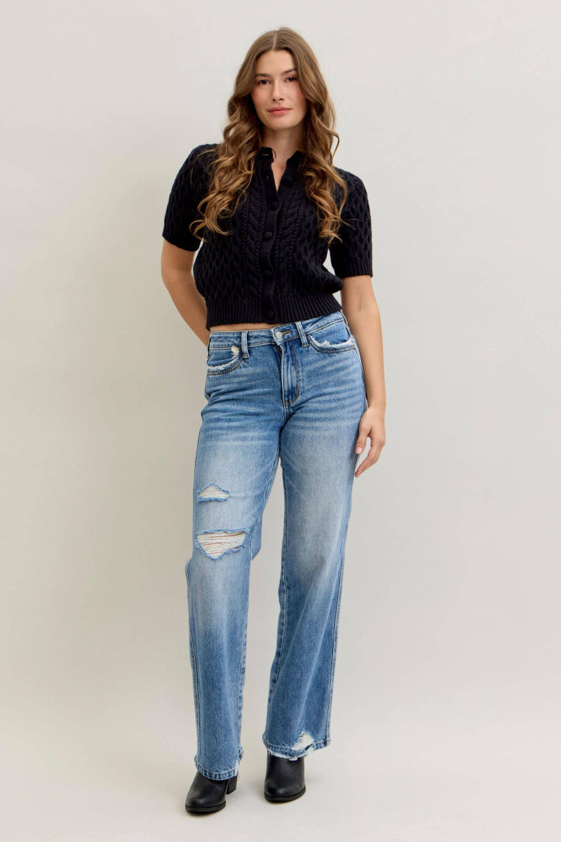 Woman wearing a black top and blue jeans against a plain background